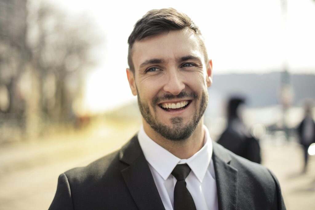 pexels-photo-3777570-3777570 A confident businessman smiling in a black suit with an outdoor background.