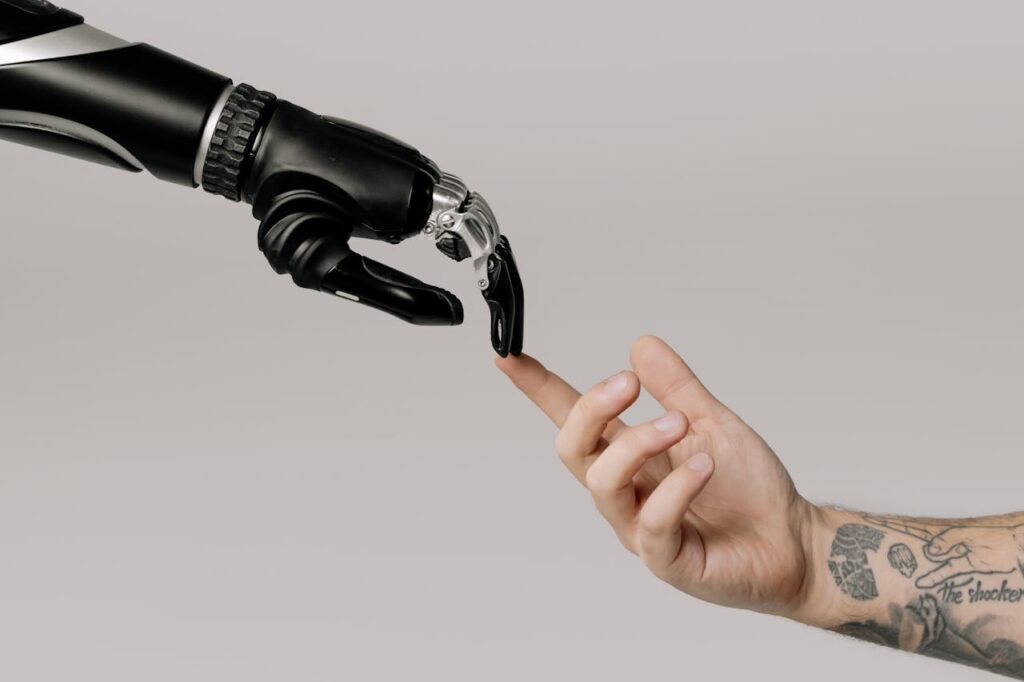 pexels-photo-6153354 A human hand with tattoos reaching out to a robotic hand on a white background.