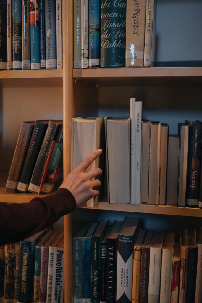 pexels-photo-8086377-8086377 A hand reaches for a book on a neatly organized wooden bookshelf.